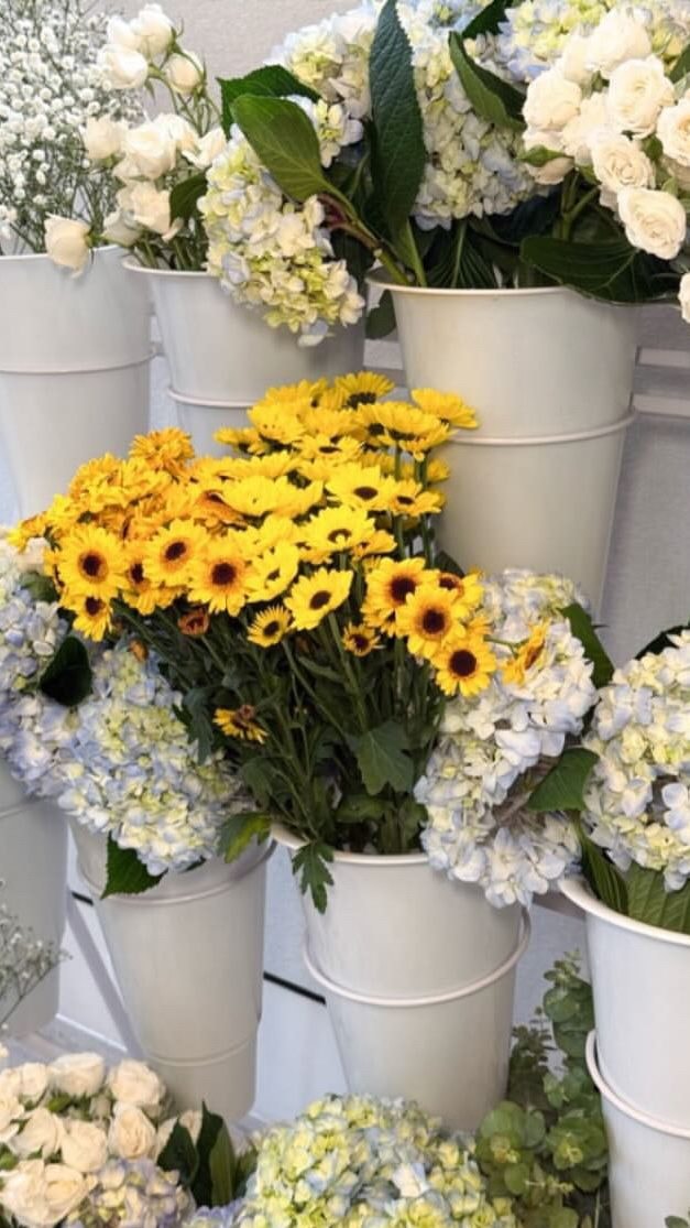 White buckets filled with sunflowers, white roses and blue and white hydrangea.