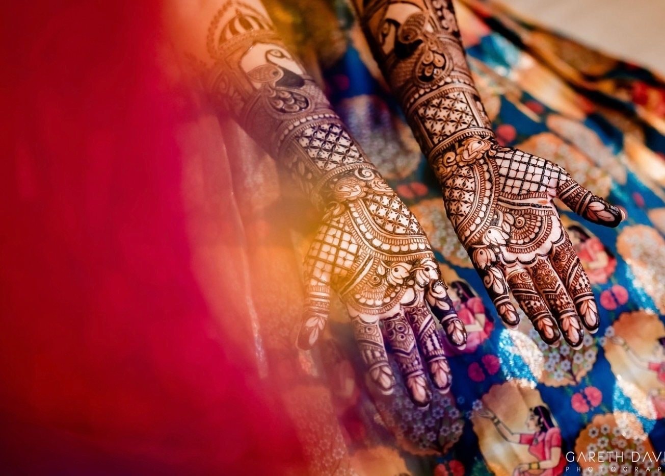 A bride’s hands covered in detailed mehndi rest over a colorful printed fabric.